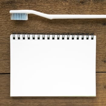 The close up of blank white notebook and the white toothbrush on wooden plank background.