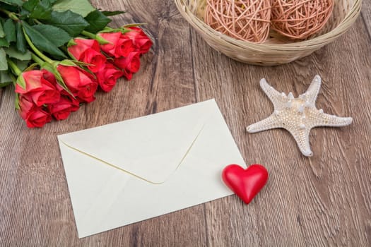 Envelope, roses and white starfish on a wooden background