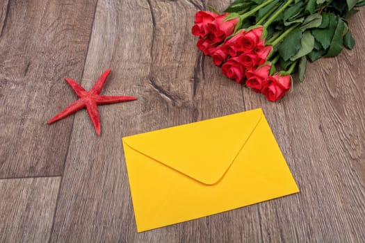 Envelope, red starfish and roses on a wooden background