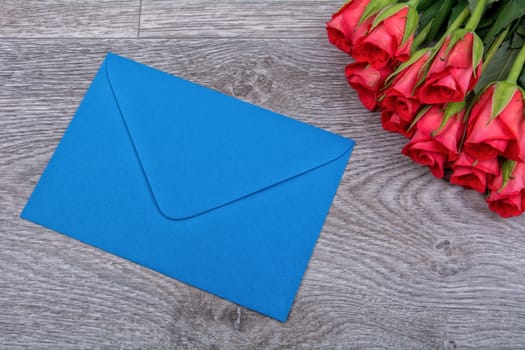 Blue envelope and red roses on a wooden background