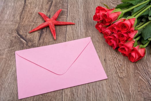 Envelope, red starfish and roses on a wooden background