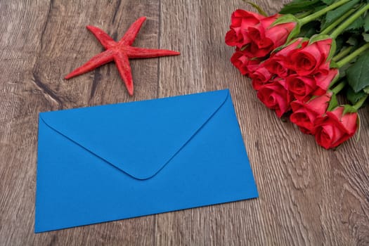 Envelope, red starfish and roses on a wooden background