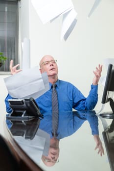 Frustrated office worker at desk throws paperwork in air
