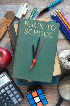 Clock hands pointing towards back to school book with school accessories 