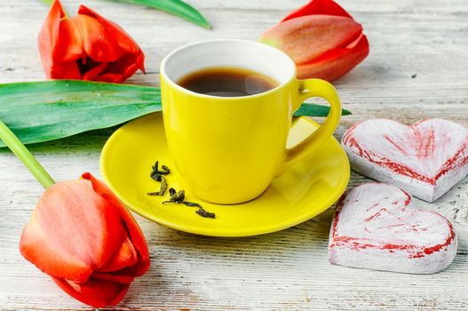 Yellow cup with tea,symbolic of the heart and a bouquet of red tulips