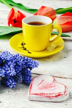 Yellow cup with tea,symbolic of the heart and a bouquet of red tulips