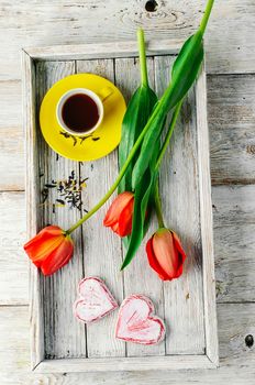 Stylish wooden tray with cup of tea and tulips in romantic style
