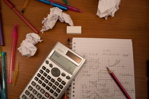 Messy table with notebook, pencils, crumpled papers and calculator