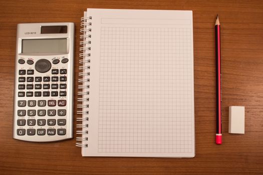 Calculator, pencil, eraser and notebook on the wooden table