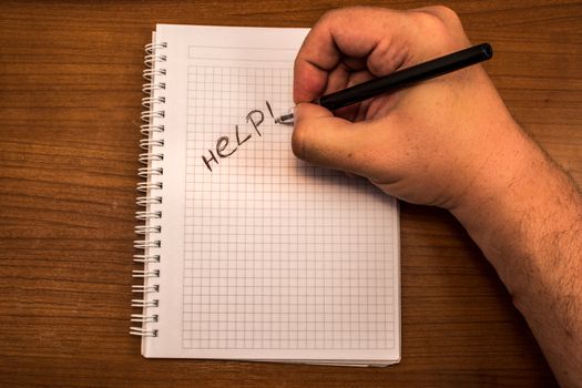 Hand with pencil and notebook. Help is written on the paper