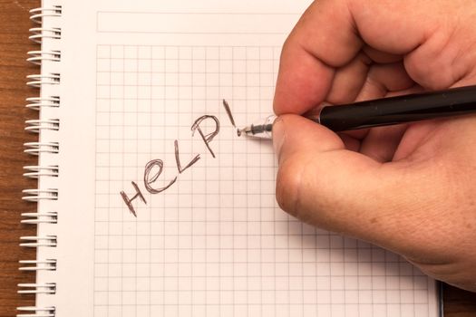 Hand with pencil and notebook. Help is written on the paper