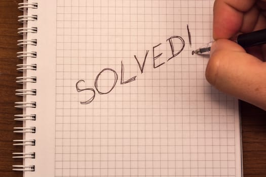 Hand with pencil and notebook. Solved is written on the paper