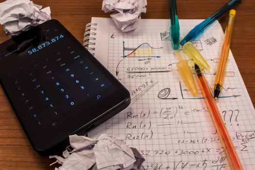 Notebook full of mathematics. Smart phone, pencils and crumpled paper are visible