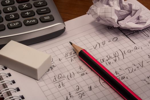 Messy table with notebook, pencils, crumpled papers and calculator
