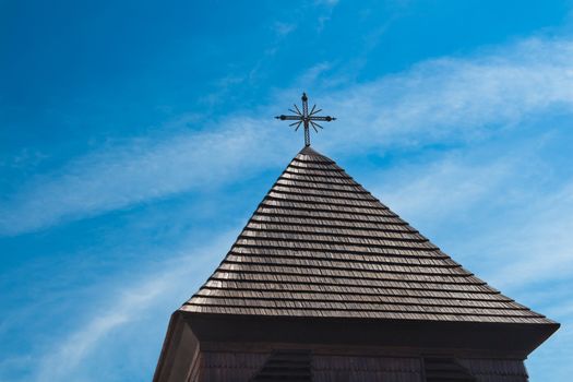 Dark brown roof made of wooden shingle with a cross on the top. Cloudy sky. Svaty Jur, Slovakia, Europe.