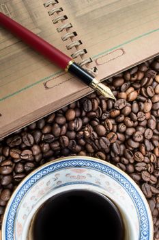 Cup of coffee, notebook and pen on coffee background