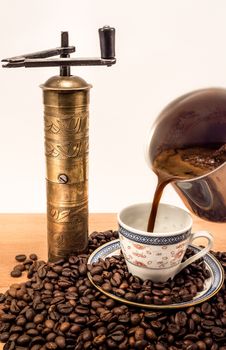 Old coffee grinder with black coffee pouirng in a coffee cup Everything is covered with coffee beans