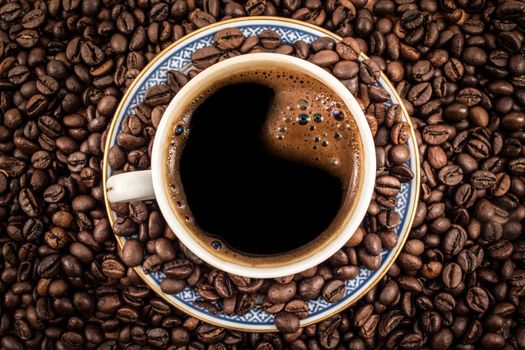 Shot of a coffee in a cup taken from above. Everything is covered with coffee beans