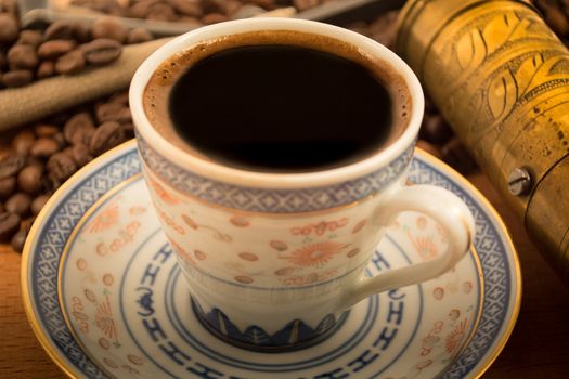 Old coffee cup with hand grinder and coffee beans in the background and