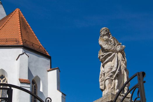 Entrance to the church of Saint George in Svaty Jur, Slovakia. Stone statue beside the gate. Walls and roof of the church on the left.Intense blue sky.