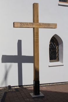 Wooden cross with a years of Saint Missions and its shadow on the wall of the gothic church in Svaty Jur, Slovakia. Traditional gothic window beside.