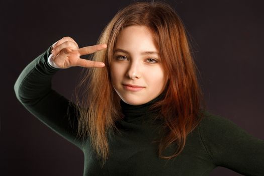 Portrait of cute girl showing peace sign with two fingers on dark background