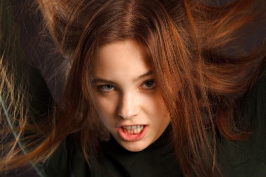 Closeup portrait of redhead woman lifting her hair on dark background