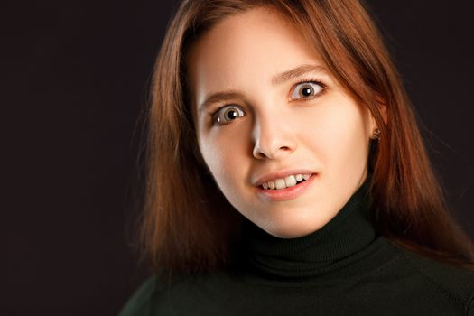 Portrait of surprised redhead woman on dark background
