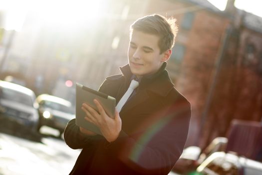 Young business man in black coat in street using tablet