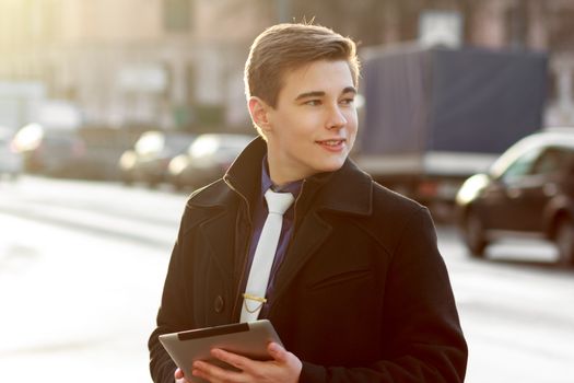 Young business man in black coat in street using tablet