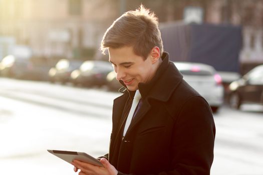 Young business man in black coat in street using tablet