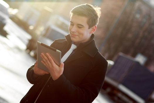 Young business man in black coat in street using tablet