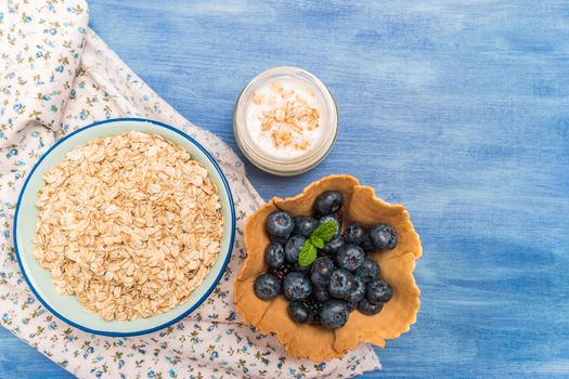 Waffle with blueberries and mint leaf. Yogurt and bowl of oatmeal  on rustic textured background. Top view with copy space.