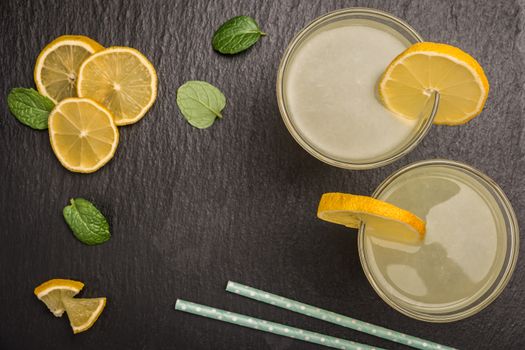 Glass of homemade lemonade with mint and lemon wedges on slate. Top view with copy space.