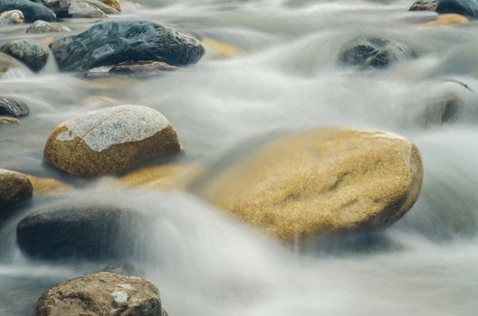 Stone is in the mountain river, blurred by a slow shutter speed