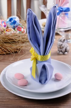 Napkin folded in the form of a hare on a plate with candy in the form of small eggs