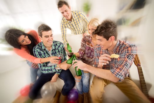 Friends at home party smiling and cheerful toast knocking with bottles and glasses.