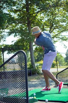 Athletic golfer swinging at the driving range dressed in casual attire.