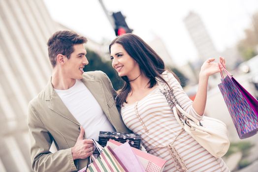 Young happiness couple crossing the crosswalk, holding hands with a bunch shopping bags.