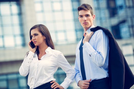 Young business couple standing in front of office buildings and business woman talking by mobile phone.