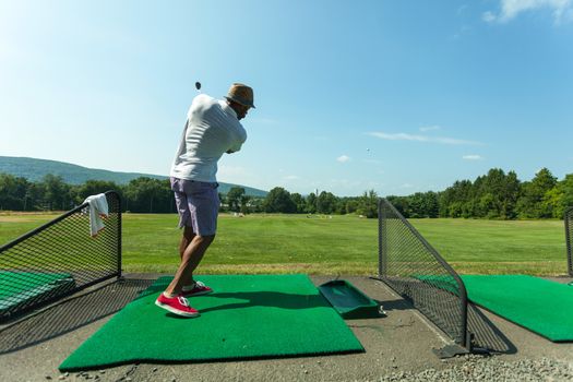 Athletic golfer swinging at the driving range dressed in casual attire.