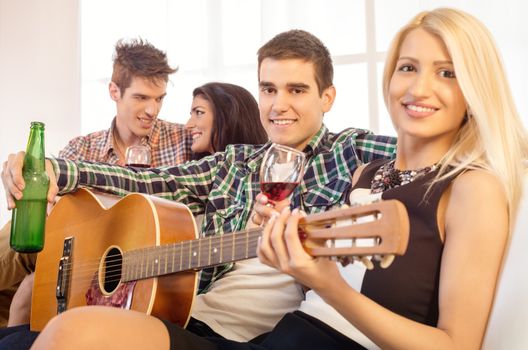 Small group of happy young people hang out at the house party with an acoustic guitar.