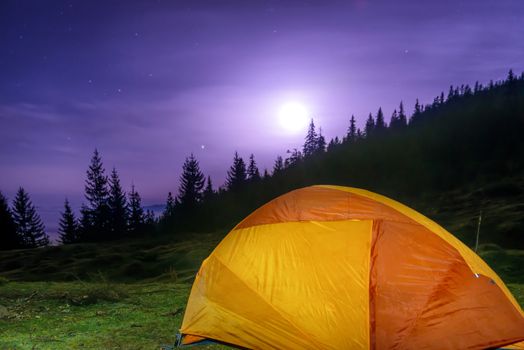 Illuminated orange camping tent under moon, stars at night