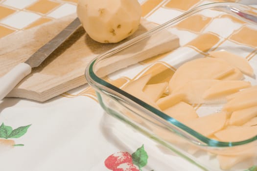 Sliced potatoes in a glass tray on a kitchen table