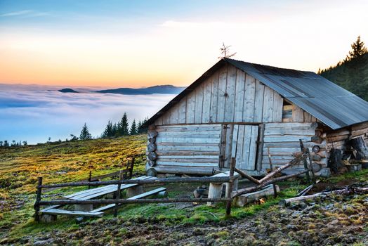 Old house in front of beautiful nature with clouds ocean, field of grass and mountains