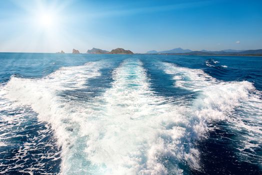 Waves on blue sea behind the speed boat water with bright sun shining on the sky