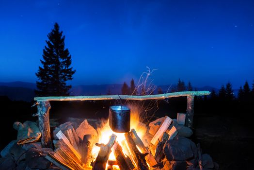 Cooking food in the pot on fire under blue night sky with many stars