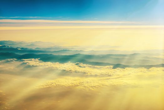 View from a plane to sunset on the sky with sunrays. Fluffy clouds background