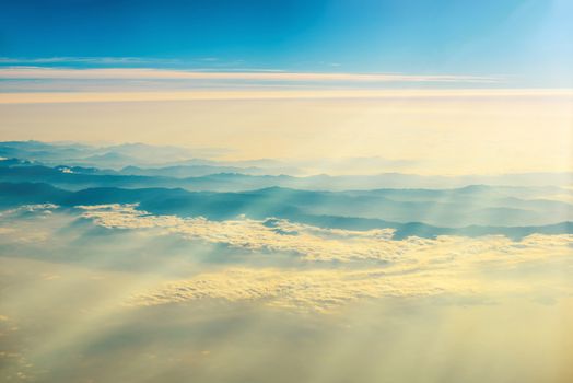 View from a plane to sunset on the sky with sunrays. Fluffy clouds background