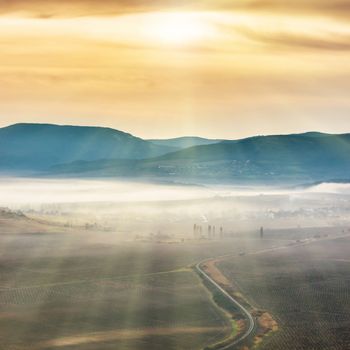 Blue mountains and road covered with mist against sunset. Bright sun shining on the sky